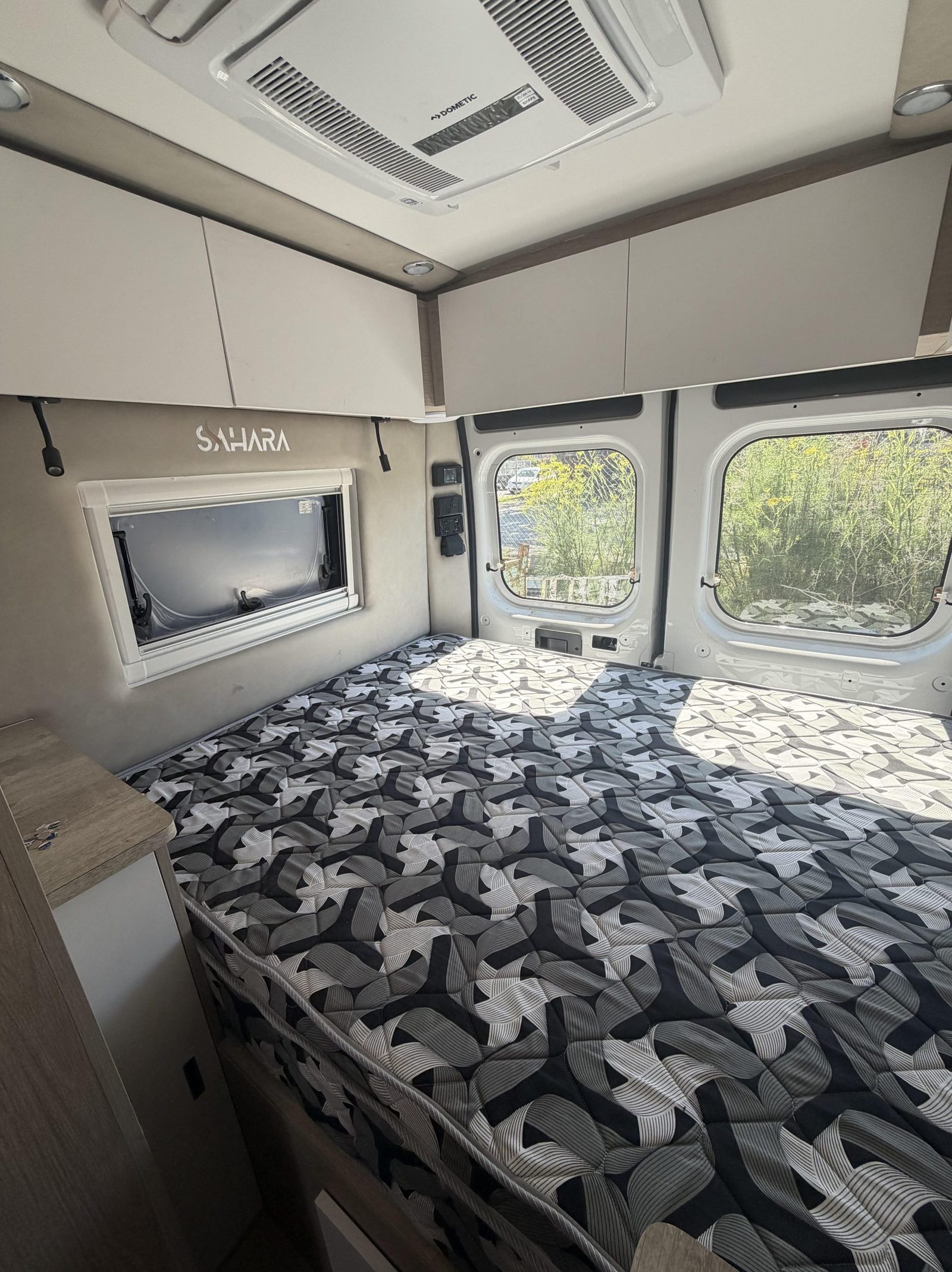 Rear bedroom with patterned quilt and large windows in a Sahara van
